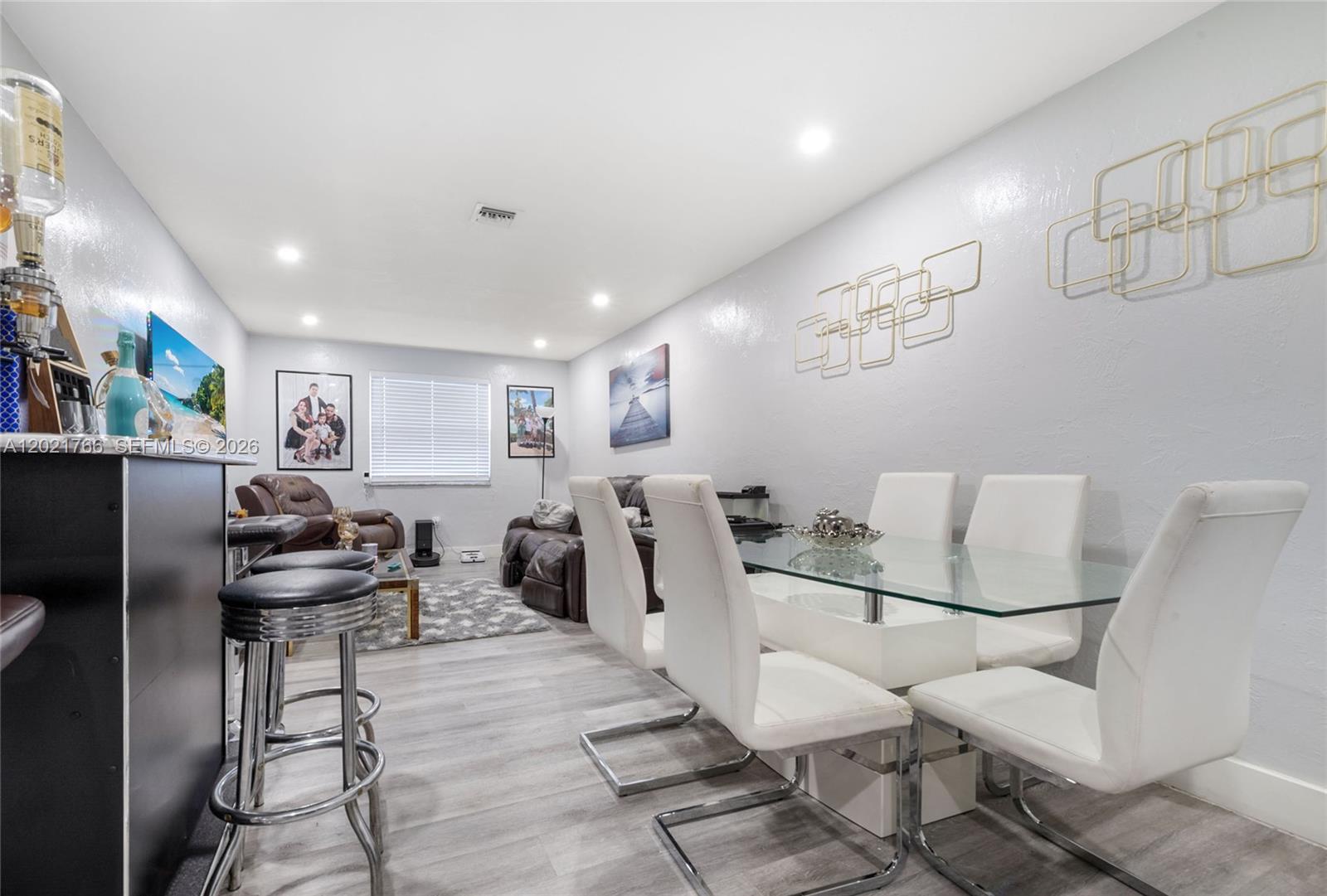 A dining area with a glass table and white chairs sits adjacent to a living space — HIALEAH, FL