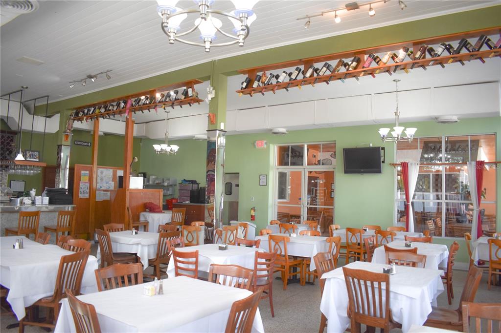 A restaurant dining room features white-clothed tables, wooden chairs, and wine bottles displayed on shelves — 1623 E 5TH AVENUE, TAMPA, FL
