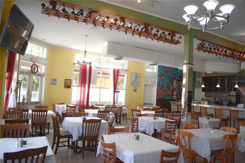A restaurant dining room features white tablecloths, wooden chairs, and wine bottles displayed on overhead racks — 1623 E 5TH AVENUE, TAMPA, FL