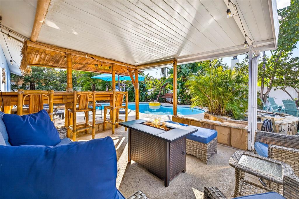 A covered patio features a bamboo tiki bar, a fire pit, and a swimming pool — 10050 84TH WAY, LARGO, FL