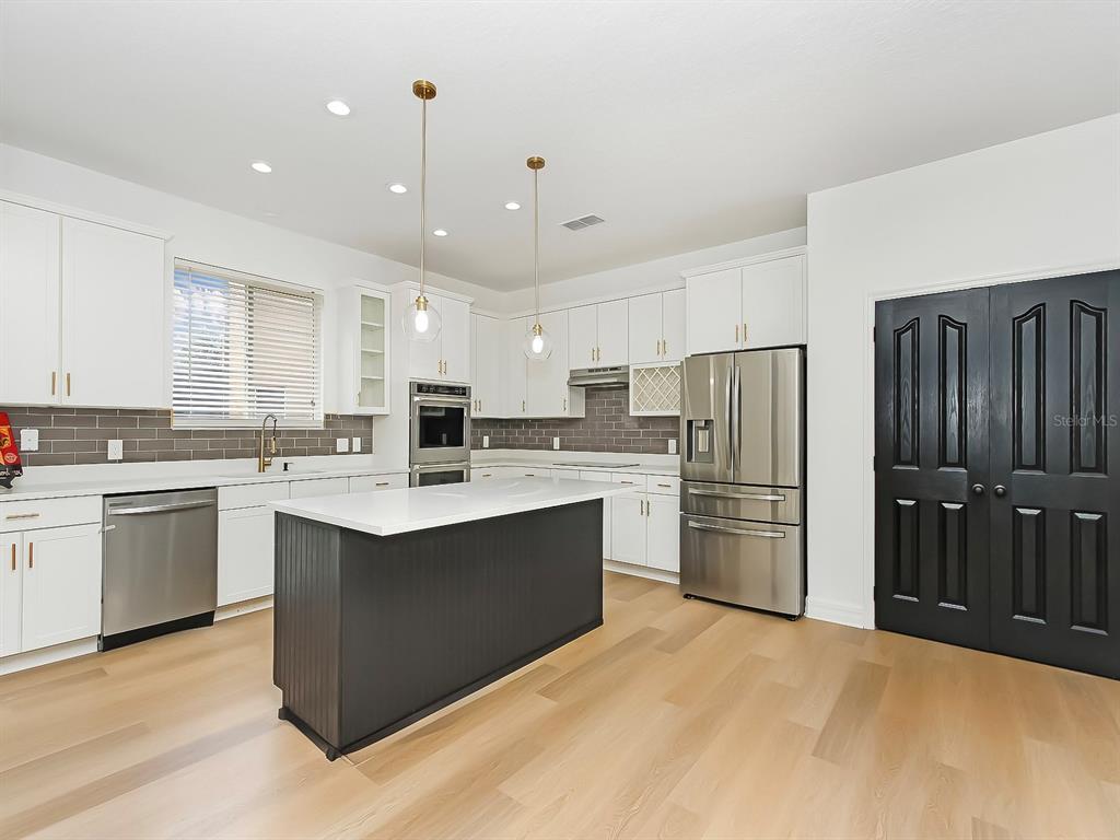 A kitchen features white cabinets, a dark island, stainless steel appliances, and light wood flooring — 13313 HALKYN POINT, ORLANDO, FL