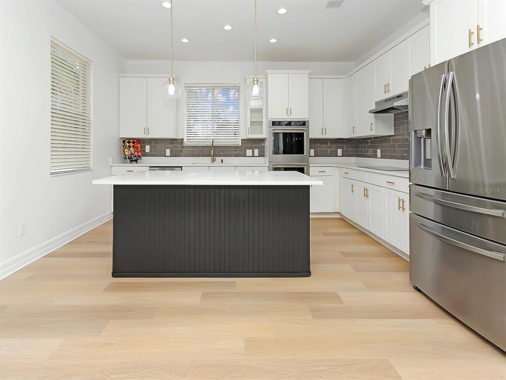 A modern kitchen features white cabinetry, a dark island, stainless steel appliances, and light wood flooring — 13313 HALKYN POINT, ORLANDO, FL