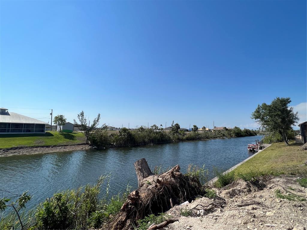 A canal flows past a grassy bank with a large tree stump in the foreground — 2204 NW 6TH PLACE, CAPE CORAL, FL