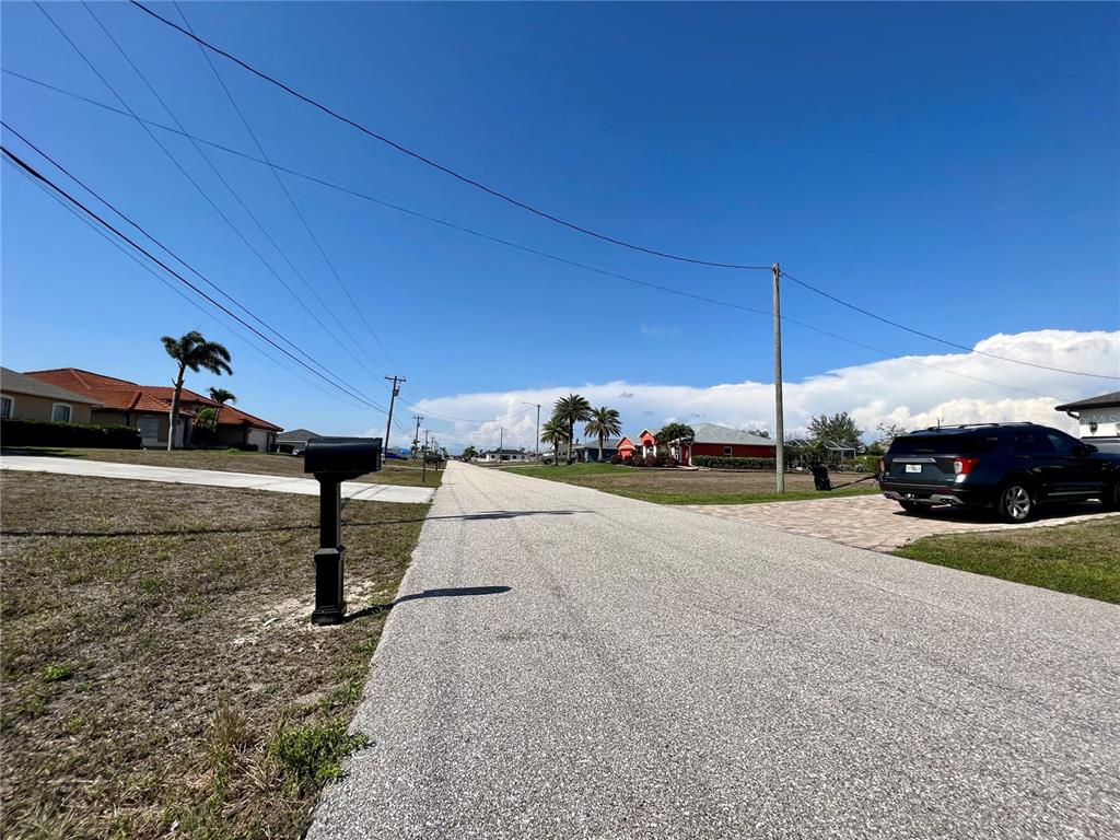 A paved residential street with houses, palm trees, and a parked SUV under a blue sky — 2204 NW 6TH PLACE, CAPE CORAL, FL