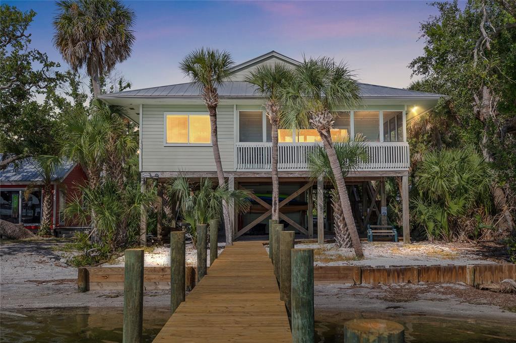 A stilt house with a wooden dock extending into the water surrounded by palm trees — 8178 LITTLE GASPARILLA ISLAND, PLACIDA, FL