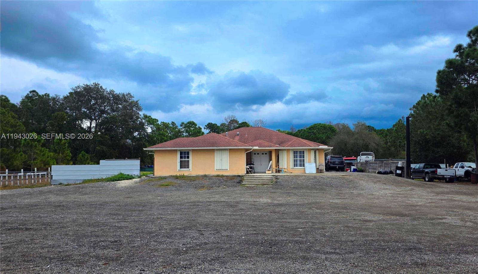 A single-story house with a tan exterior and a brown roof sits on a gravel lot — 355 N Lindero ST, Clewiston FL 33440, CLEWISTON, FL