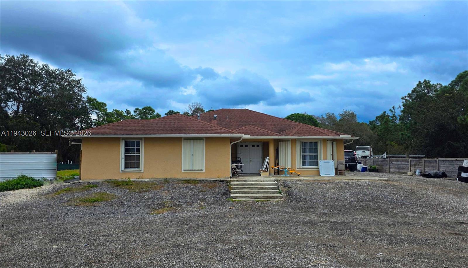 A single-story tan house with a brown roof sits on a large gravel lot — 355 N Lindero ST, Clewiston FL 33440, CLEWISTON, FL