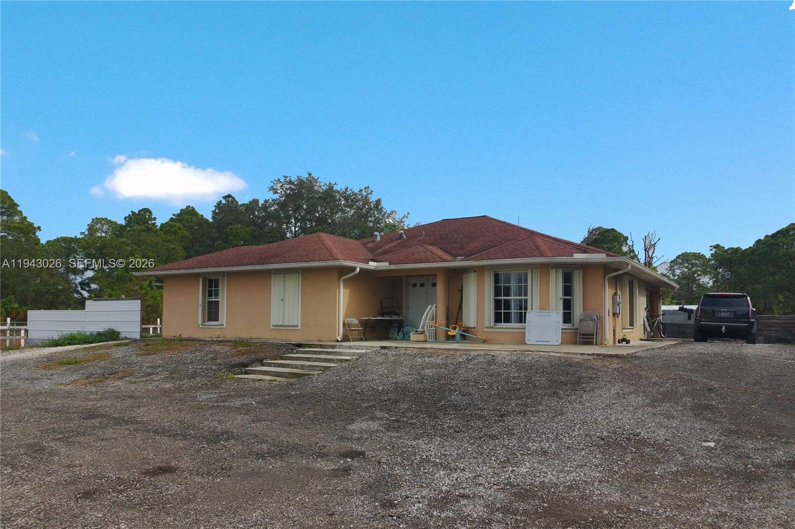 A single-story, tan-colored house with a red roof sits on a large gravel lot — 355 N Lindero ST, Clewiston FL 33440, CLEWISTON, FL