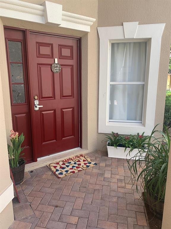 A red front door with a side window and a brick patio entrance — 6956 BRESCIA WAY, ORLANDO, FL