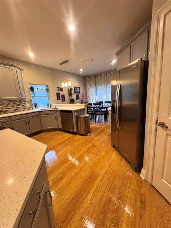 A kitchen features gray cabinets, stainless steel appliances, and light wood flooring — 6956 BRESCIA WAY, ORLANDO, FL