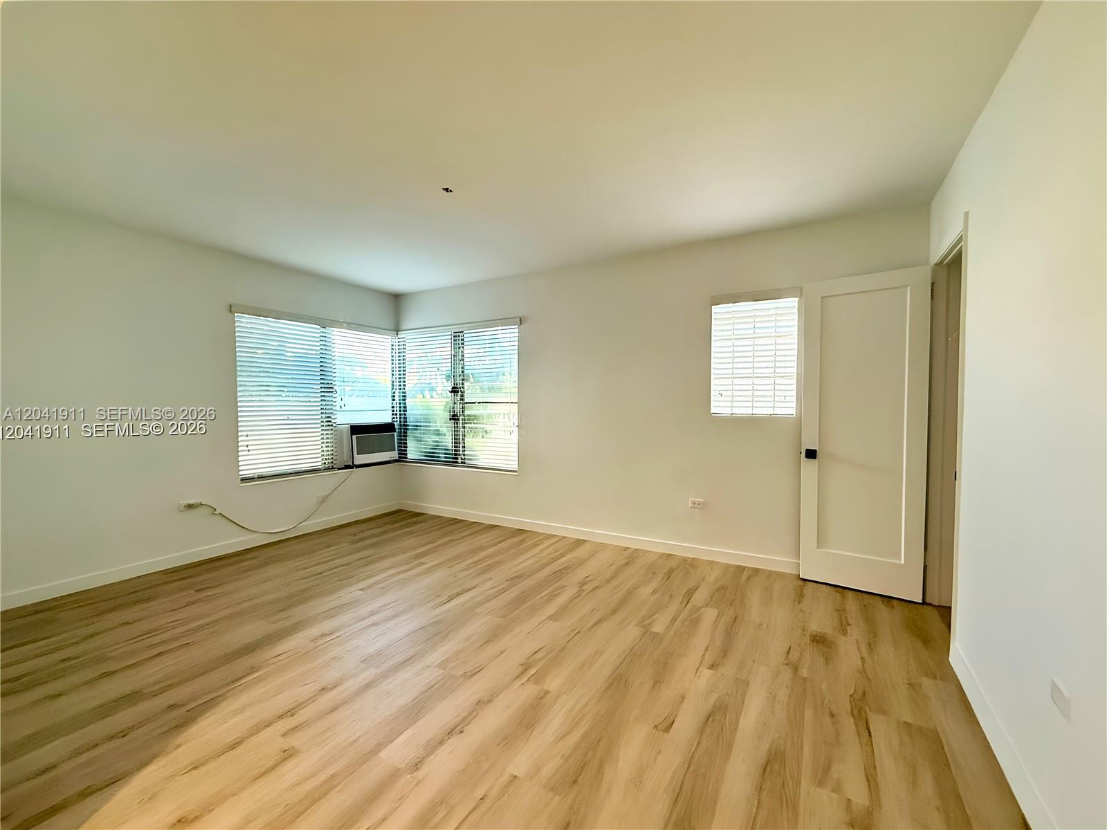 An empty room features light wood-look flooring, white walls, and two windows with blinds — 641 10th St # 2, Miami Beach FL 33139, MIAMI BEACH, FL