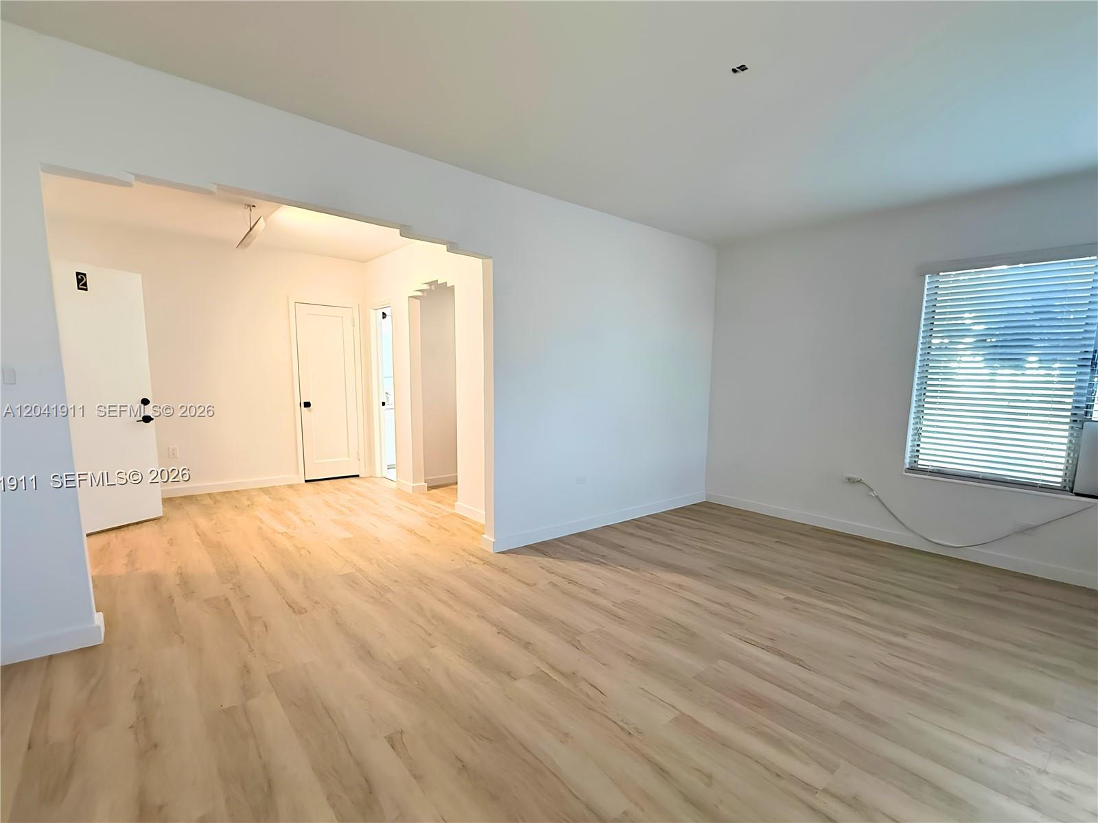 An empty room features light wood-look flooring, white walls, and an arched entryway — 641 10th St # 2, Miami Beach FL 33139, MIAMI BEACH, FL