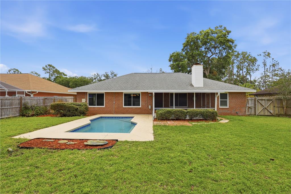 The backyard features a brick house with a swimming pool, a screened porch, and lawn — 77 BRUNING LANE, PALM COAST, FL