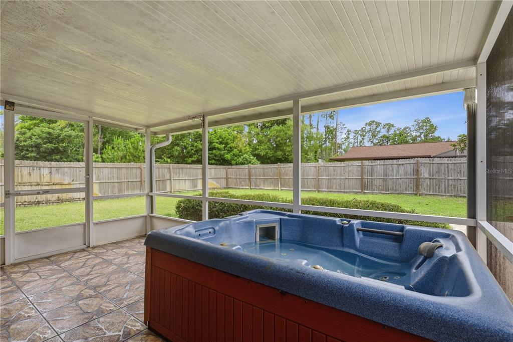 A screened-in patio features a blue hot tub on a tiled floor overlooking a backyard — 77 BRUNING LANE, PALM COAST, FL