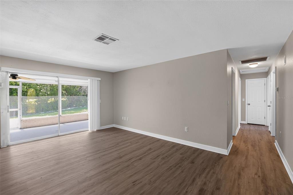 An empty living room with wood-look flooring, beige walls, and a sliding glass door — 2140 N BAY HILLS BOULEVARD, SAFETY HARBOR, FL