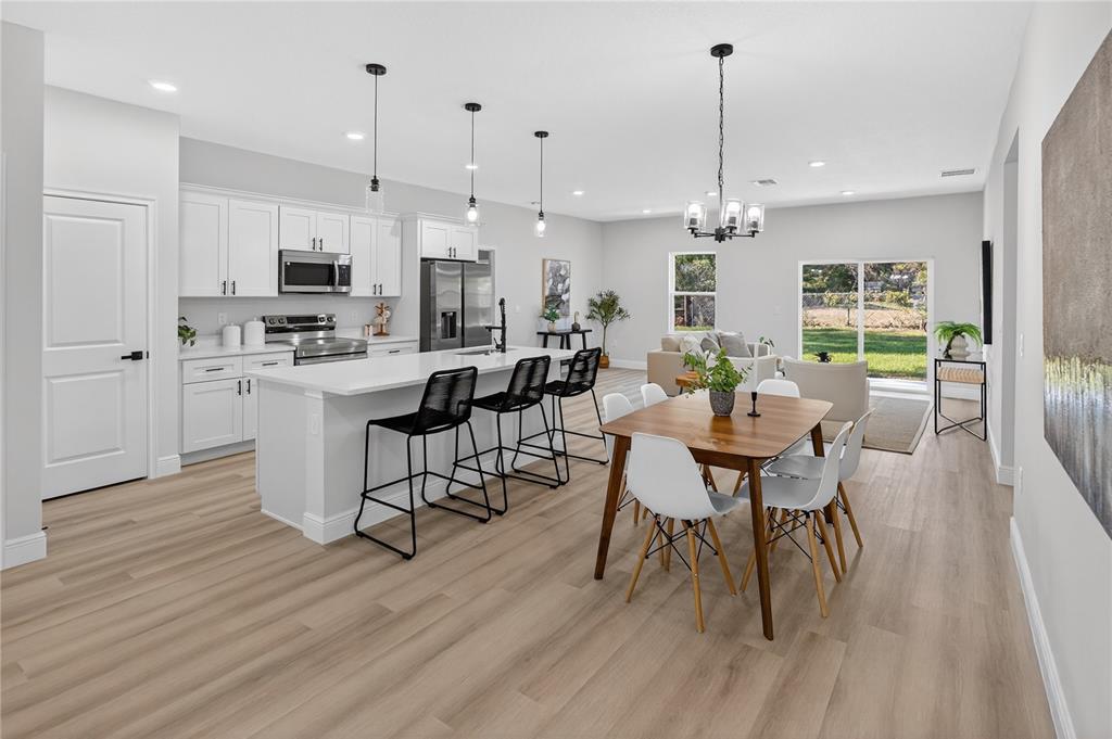 An open-concept kitchen and dining area features white cabinetry, a central island, and wood flooring — 8002 N MALTESE DRIVE, DUNNELLON, FL