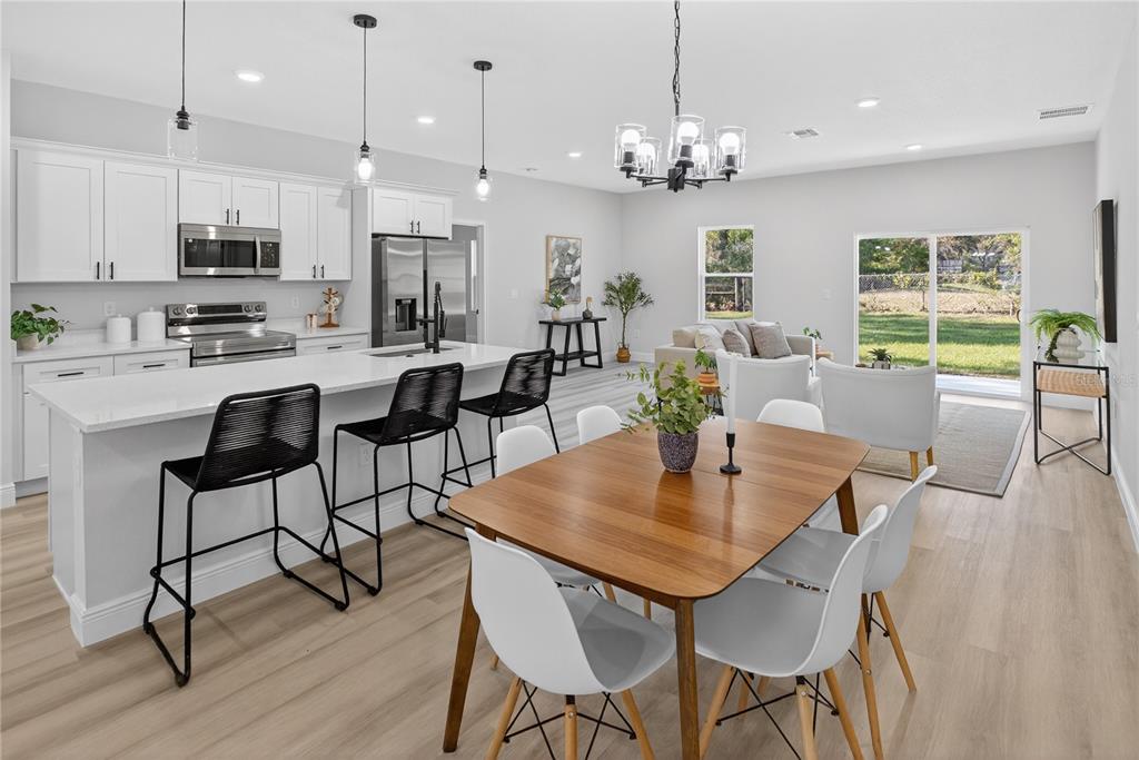 An open-concept kitchen and dining area features white cabinetry, a large island, and wood flooring — 8002 N MALTESE DRIVE, DUNNELLON, FL