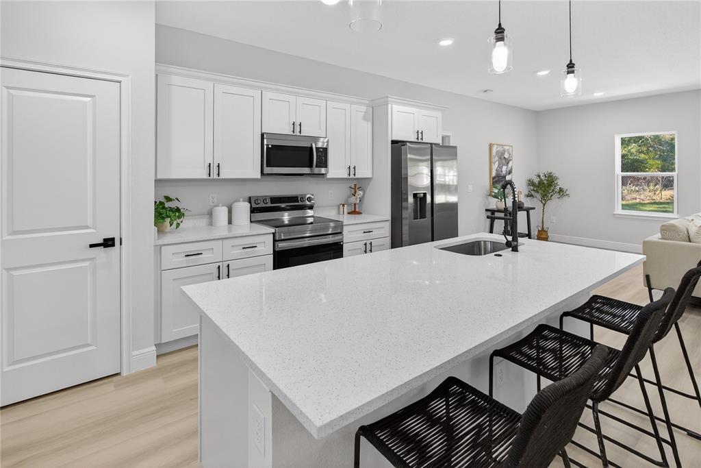 A modern kitchen features white cabinetry, a large quartz island, and black bar stools — 8002 N MALTESE DRIVE, DUNNELLON, FL