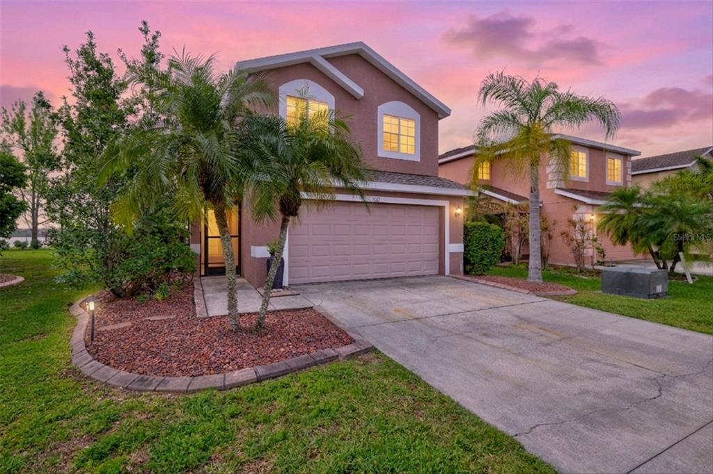 A two-story suburban house with a concrete driveway, palm trees, and a sunset sky — 7121 CHATUM LIGHT RUN, BRADENTON, FL
