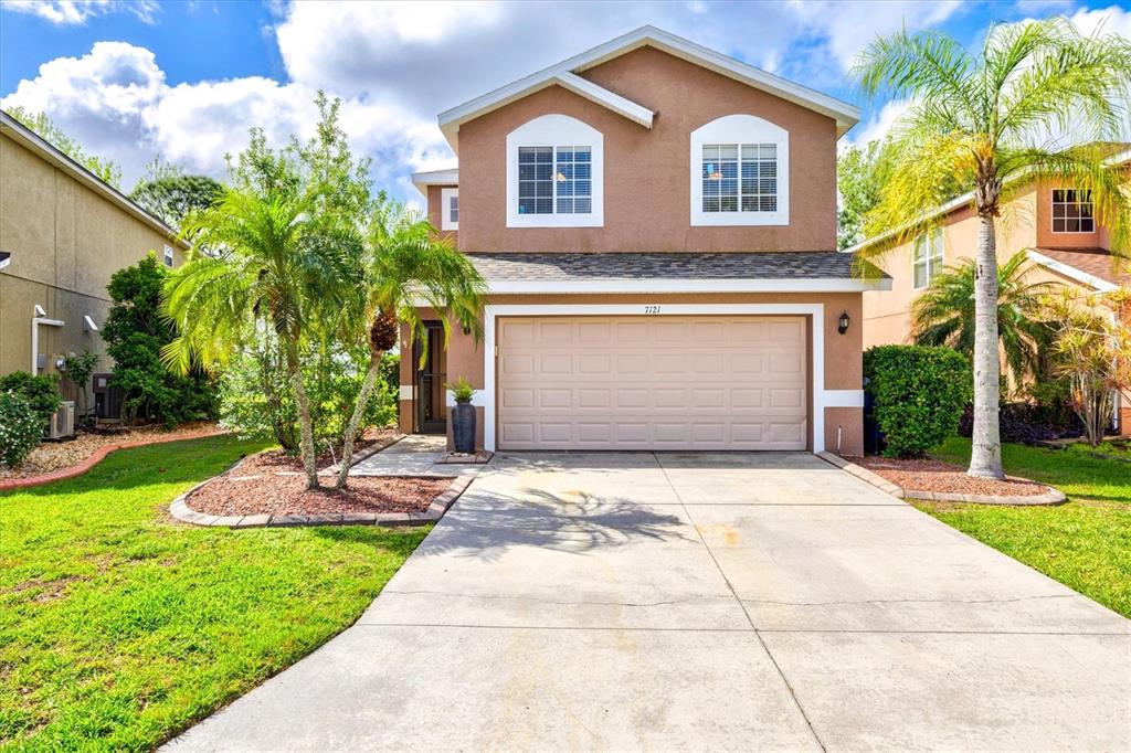 A two-story suburban house features a tan stucco exterior, a two-car garage, and palm trees — 7121 CHATUM LIGHT RUN, BRADENTON, FL