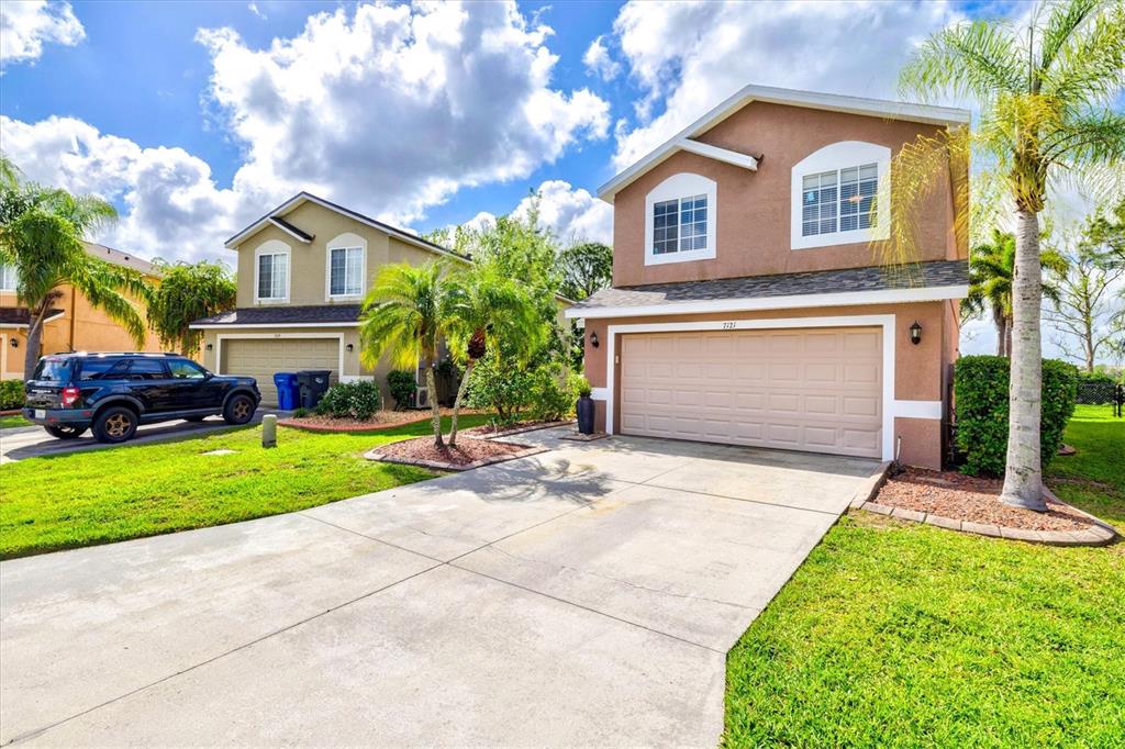 Two-story suburban houses with beige stucco exteriors, attached garages, and palm trees under a cloudy sky — 7121 CHATUM LIGHT RUN, BRADENTON, FL