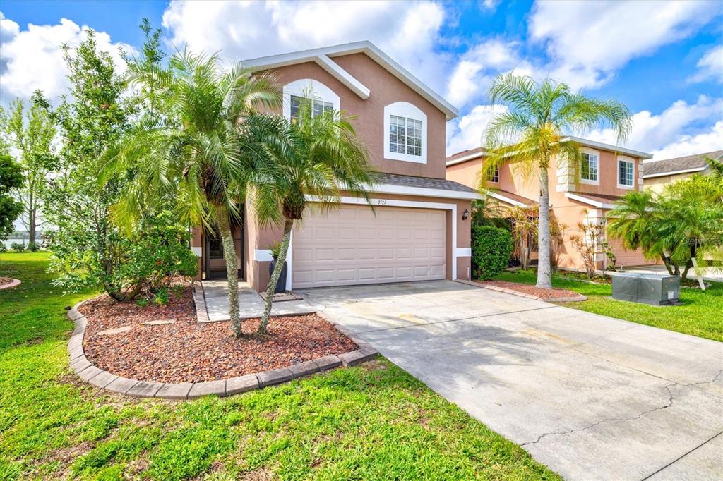 A two-story tan house with a two-car garage, palm trees, and a concrete driveway — 7121 CHATUM LIGHT RUN, BRADENTON, FL