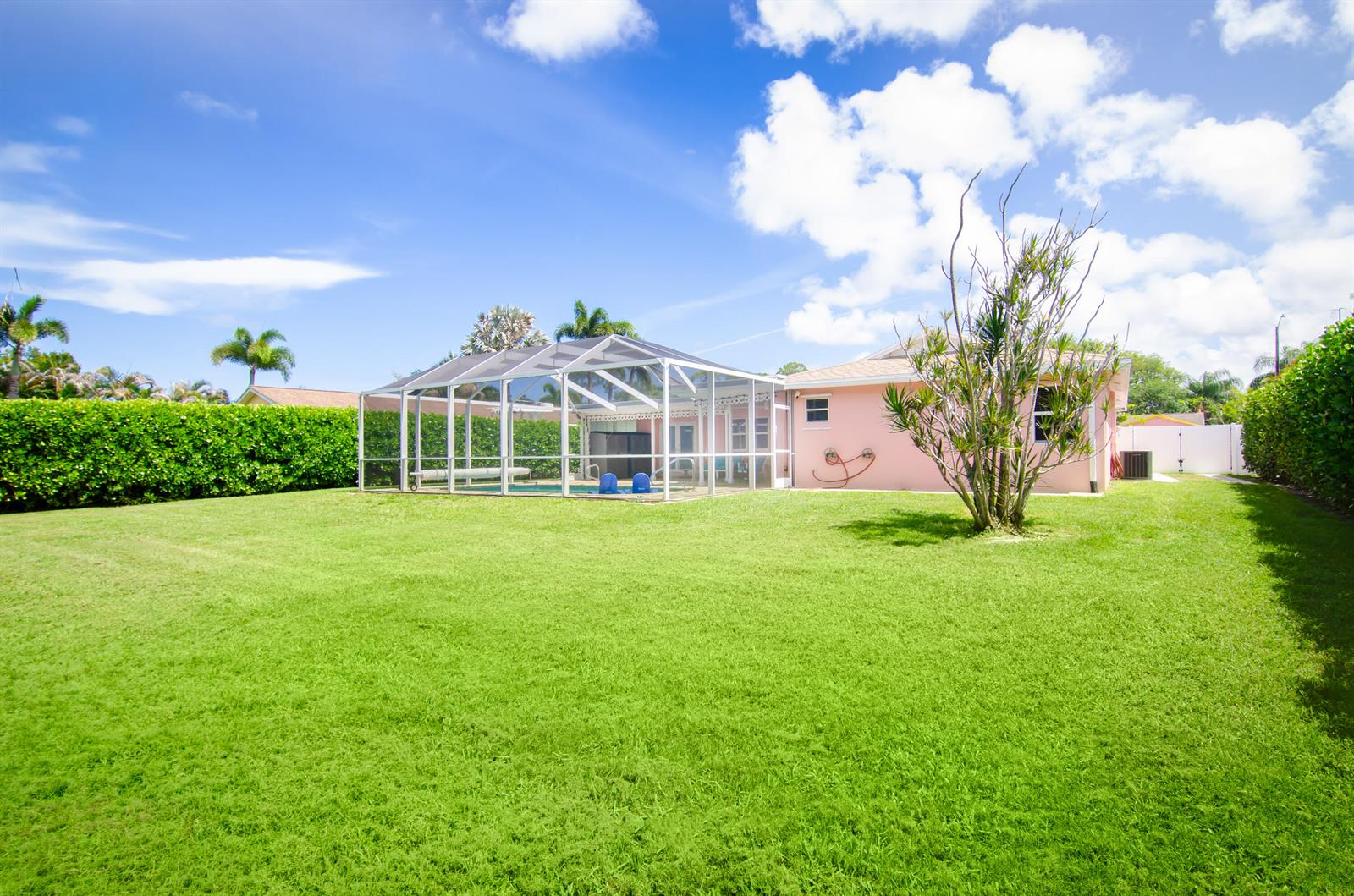 A pink house with a screened-in pool enclosure sits in a large, grassy backyard — 613 Oak Terrace, Jupiter FL 33458, JUPITER, FL