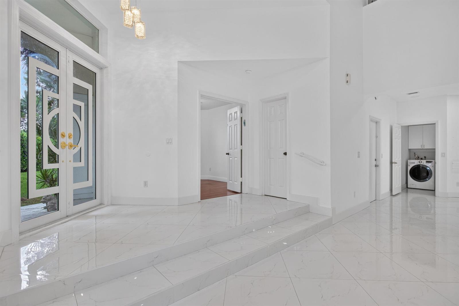 A bright foyer features white tiled floors, a step-up entry, and a laundry room visible — 7087 NW 78th Place, Parkland FL 33067, PARKLAND, FL