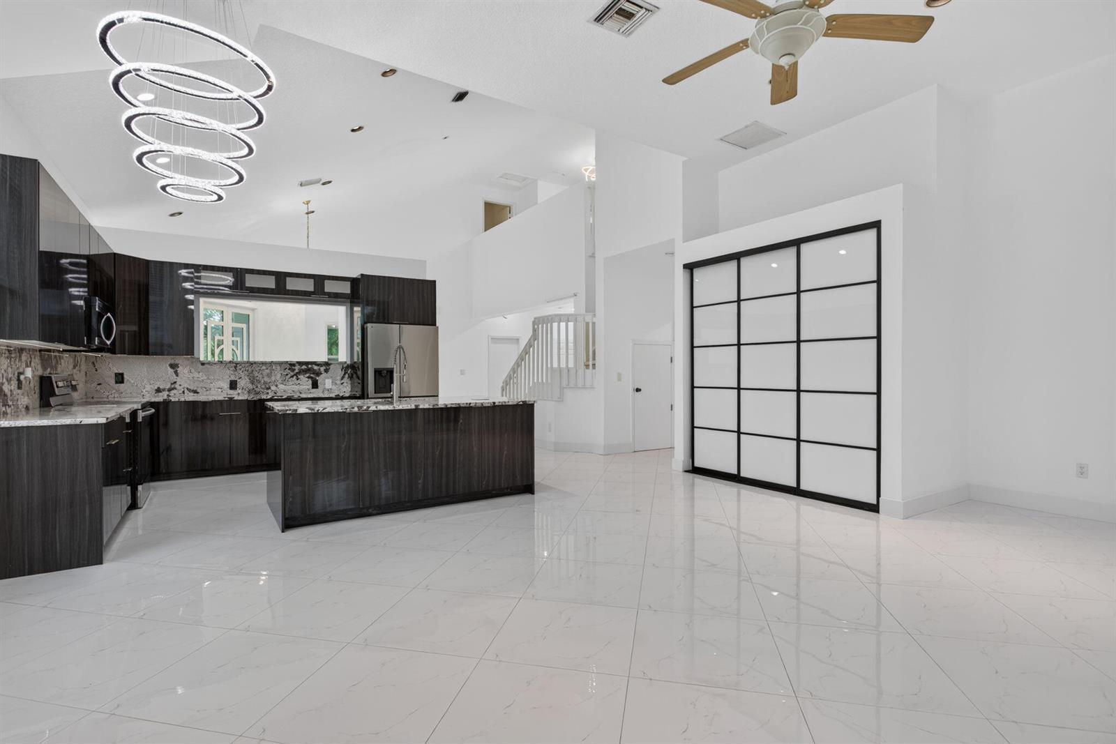 A modern kitchen with dark cabinetry and a large island opens to a spacious living area — 7087 NW 78th Place, Parkland FL 33067, PARKLAND, FL