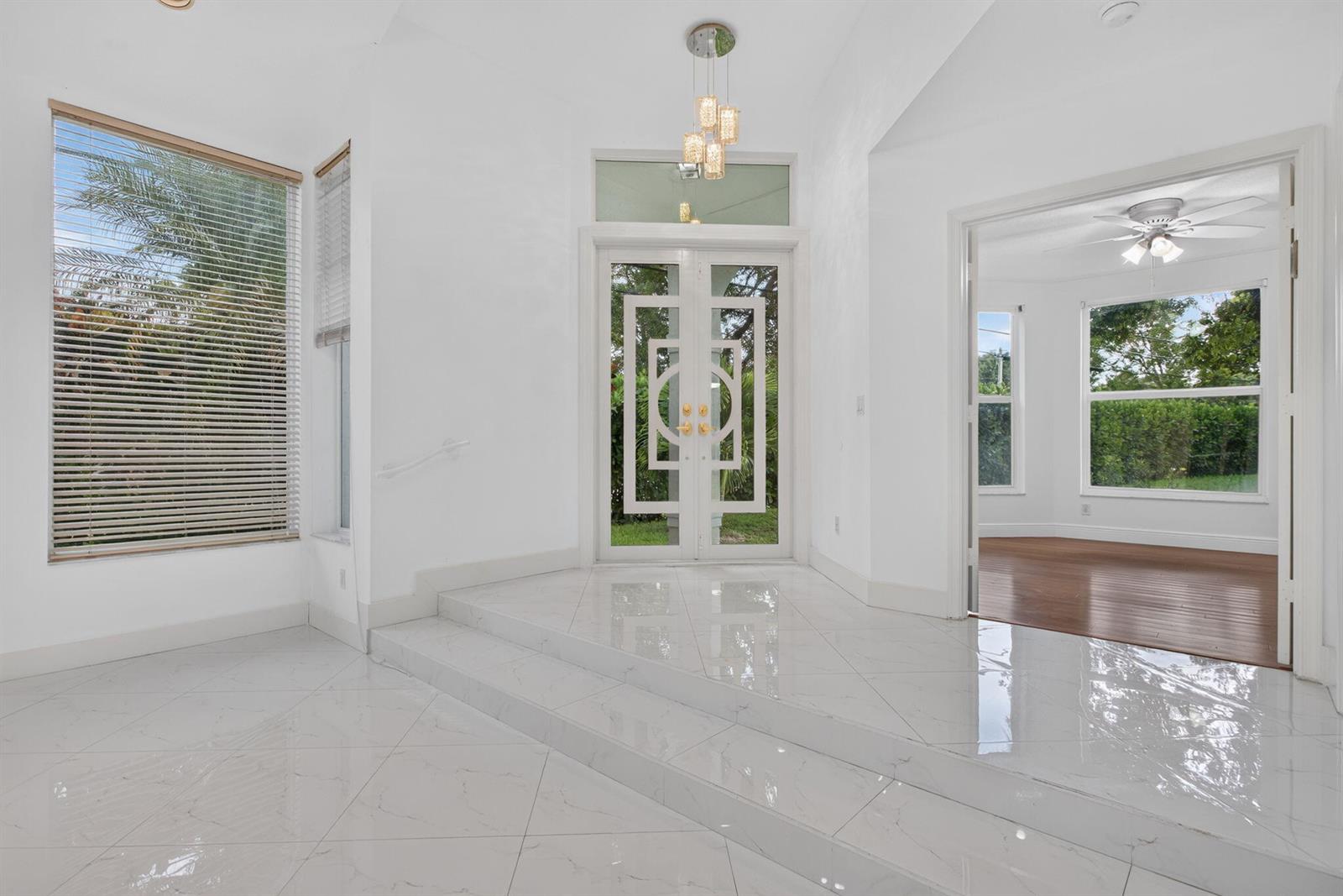 A bright entryway features white tile floors, a stepped platform, and a decorative double door — 7087 NW 78th Place, Parkland FL 33067, PARKLAND, FL