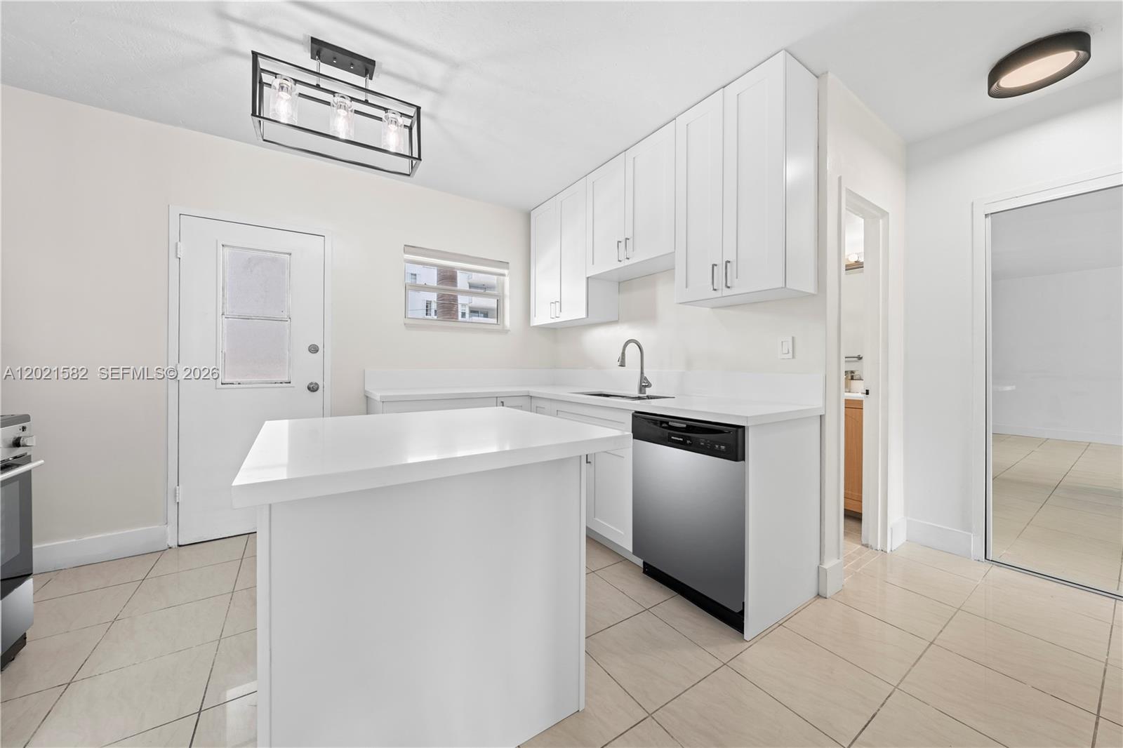 A bright kitchen features white cabinets, a small island, and light-colored tile flooring — 1300 Lincoln Rd # D204, Miami Beach FL 33139, MIAMI BEACH, FL