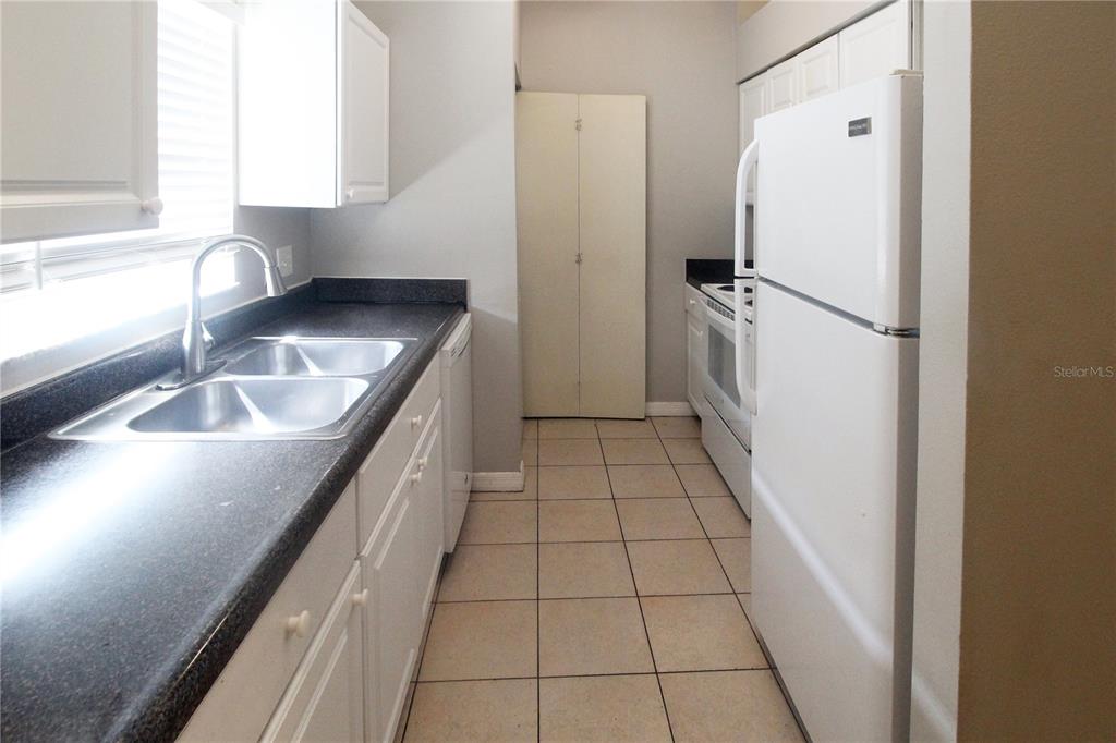 A galley-style kitchen features white cabinets, dark countertops, a white refrigerator, and tiled flooring — 864 HAND AVE, SARASOTA, FL