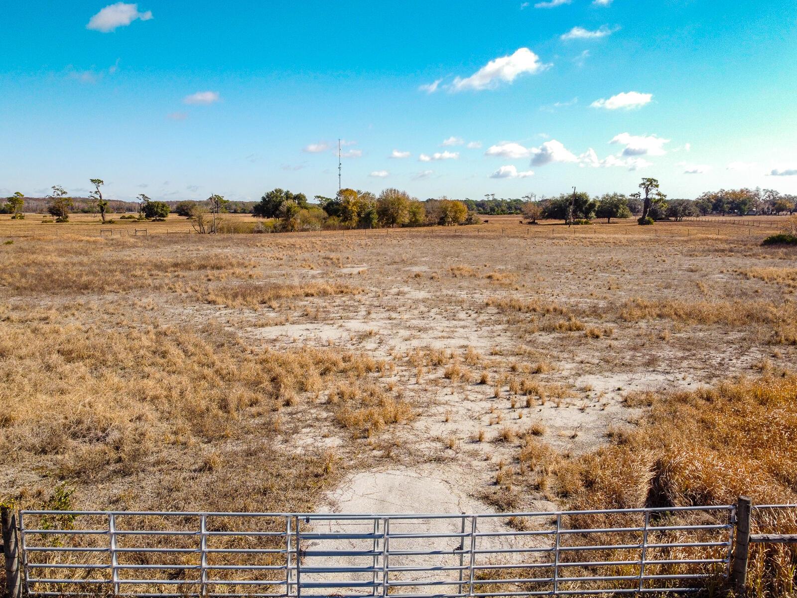 A metal gate opens to a large, dry, grassy field under a clear blue sky — 5151 S Kenansville Road, Okeechobee FL 34972, OKEECHOBEE, FL