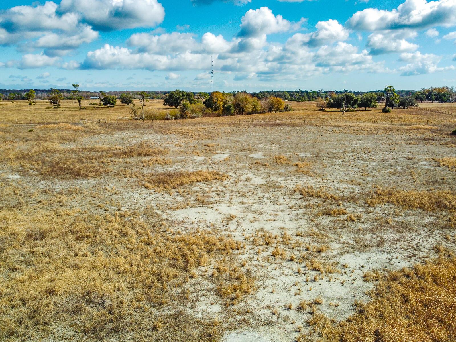 An aerial view of a large, dry, grassy field under a bright blue cloudy sky — 5151 S Kenansville Road, Okeechobee FL 34972, OKEECHOBEE, FL