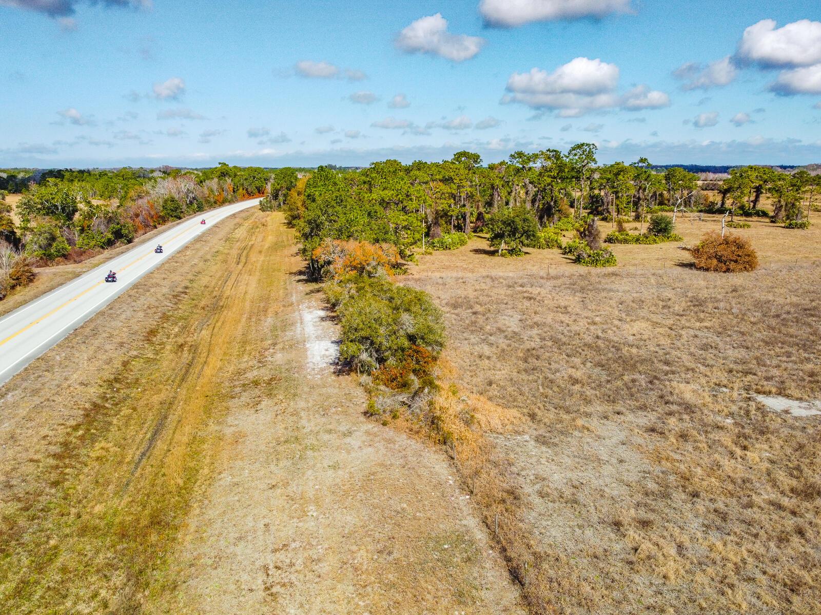 An aerial view shows a paved road running alongside a grassy field and wooded area — 5151 S Kenansville Road, Okeechobee FL 34972, OKEECHOBEE, FL