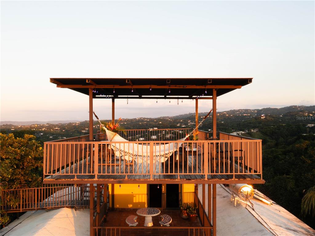 An elevated wooden deck features a hammock under a roof with a scenic mountain view — CARR. 414 KM 1.8 INT THE TERRACES, RINCON, PR