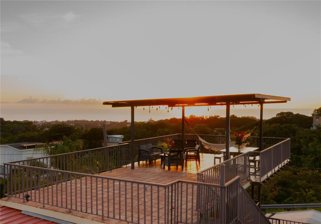 An elevated outdoor deck features a covered seating area with patio furniture overlooking a sunset — CARR. 414 KM 1.8 INT THE TERRACES, RINCON, PR