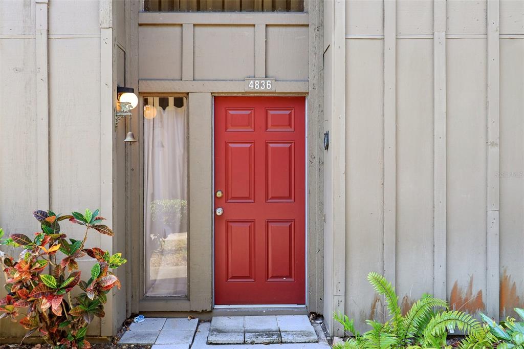 A red front door is centered on a tan exterior wall with a side window — 4836 PEBBLE BEACH DRIVE, ORLANDO, FL