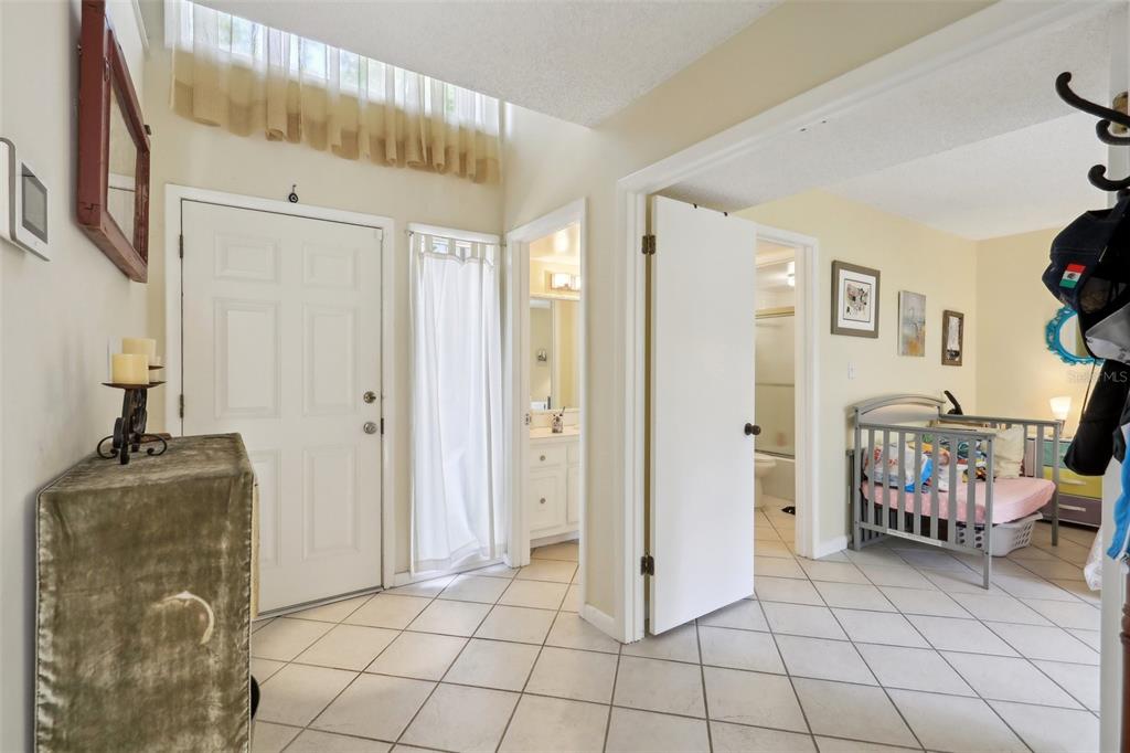 An entryway with white tile floors leads to a bathroom and a bedroom with a crib — 4836 PEBBLE BEACH DRIVE, ORLANDO, FL