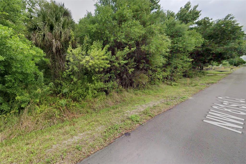 An aerial view shows a vacant, tree-covered residential lot outlined in teal — 7469 NW 81ST COURT, OKEECHOBEE, FL