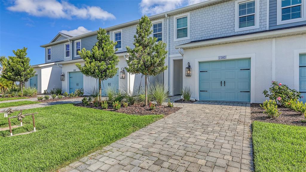 A row of townhouses with light blue garage doors and paved driveways under a blue sky — 2360 WASHINGTON PALM COURT, BRADENTON, FL