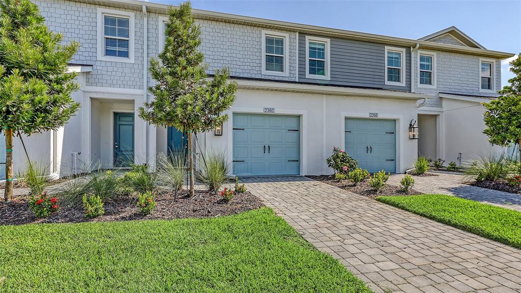 A two-story townhouse exterior features light blue garage doors, white siding, and a paver driveway — 2360 WASHINGTON PALM COURT, BRADENTON, FL
