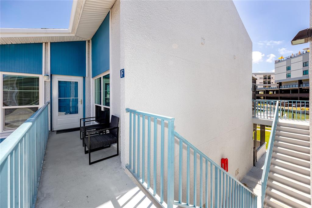 An exterior view of a balcony with blue railings, a white door, and outdoor chairs — 159 MEDALLION BOULEVARD UNIT F, MADEIRA BEACH, FL