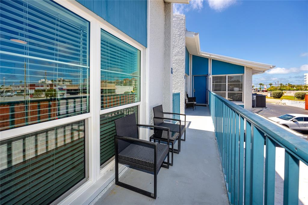 An outdoor balcony with two black chairs, blue railings, and large windows — 159 MEDALLION BOULEVARD UNIT F, MADEIRA BEACH, FL