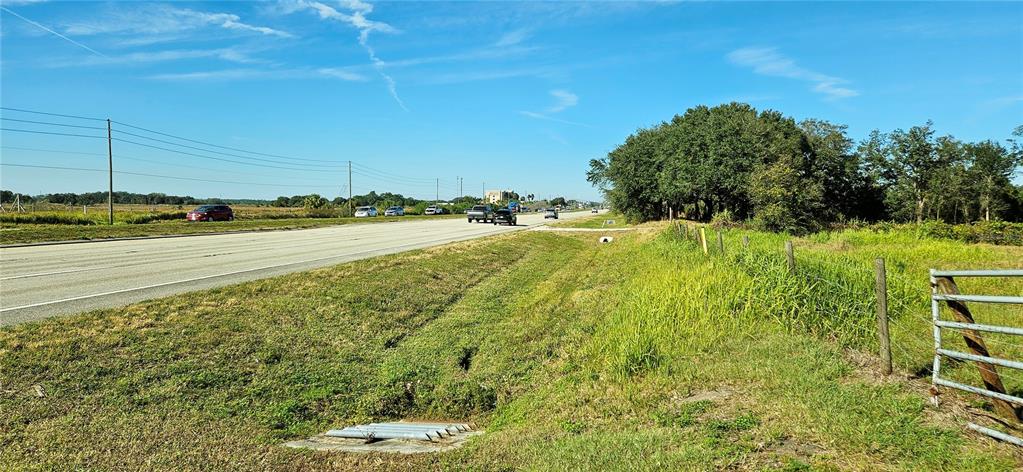 A paved road runs alongside a grassy field with a metal gate and drainage pipe — US-27, LAKE WALES, FL