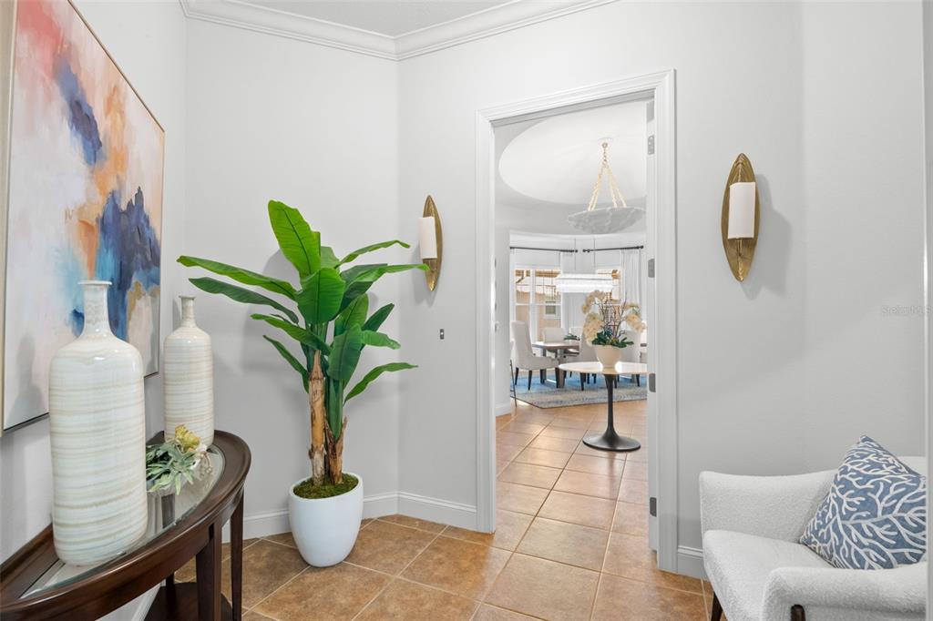 A foyer features tile flooring, a potted plant, wall sconces, and a view into a dining room — 6 ACADEMY WAY S UNIT 23A, ST PETERSBURG, FL