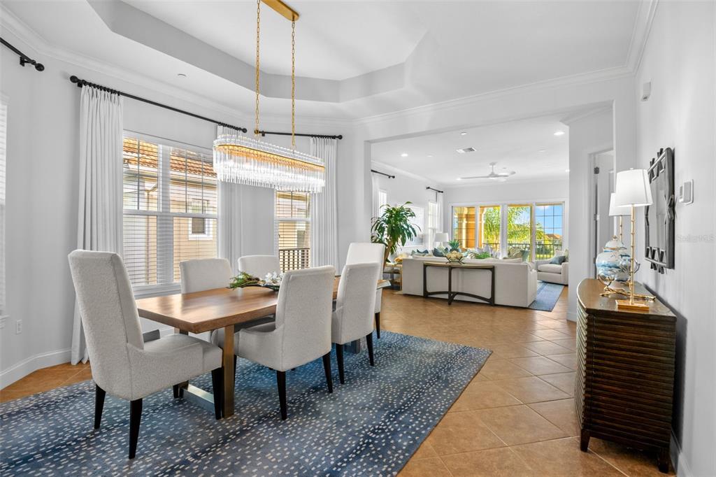 A dining room with a wooden table and chandelier opens into a bright living area — 6 ACADEMY WAY S UNIT 23A, ST PETERSBURG, FL