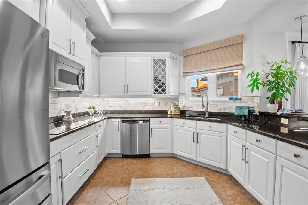 A kitchen features white cabinets, dark granite countertops, stainless steel appliances, and tile flooring — 6 ACADEMY WAY S UNIT 23A, ST PETERSBURG, FL