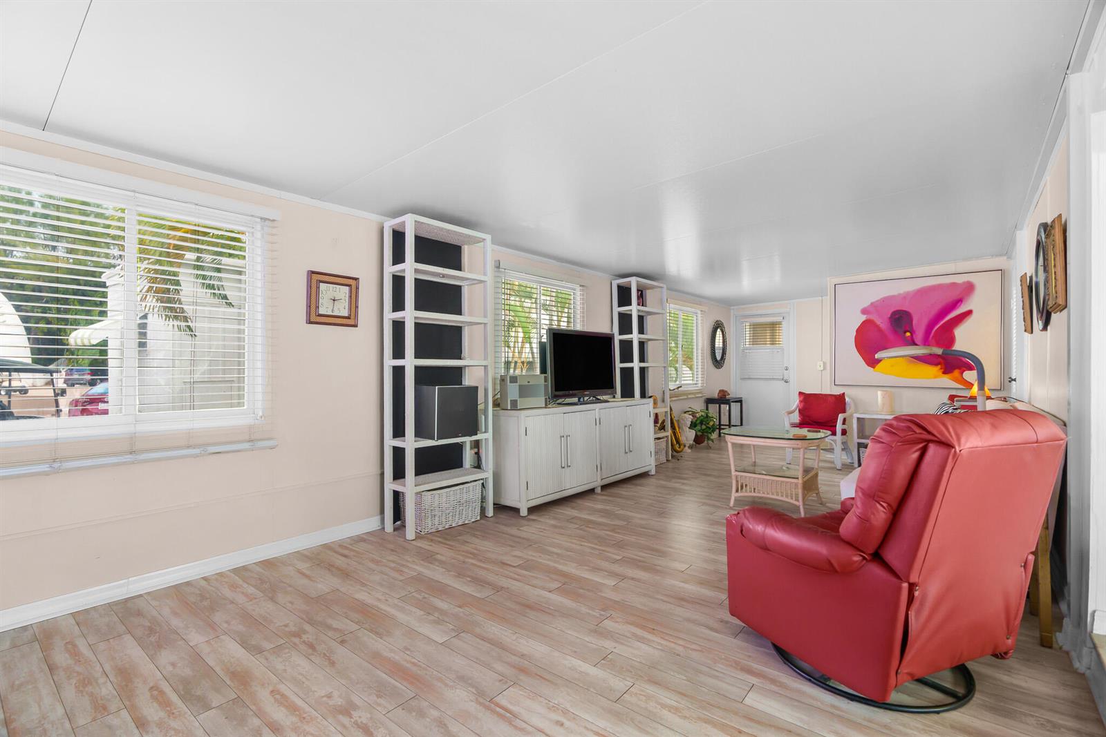 A living room features light wood-look flooring, a red recliner, white shelving, and a television — 202 N Ibis, Briny Breezes FL 33435, BRINY BREEZES, FL