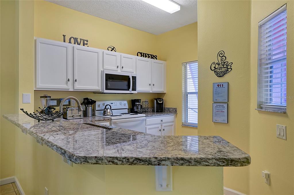 A kitchen features white cabinets, granite countertops, a breakfast bar, and yellow walls — 2767 SUN KEY PLACE, KISSIMMEE, FL